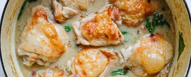 A wide pan of golden roasted chicken thighs resting on creamy cannellini beans with fennel and pancetta.