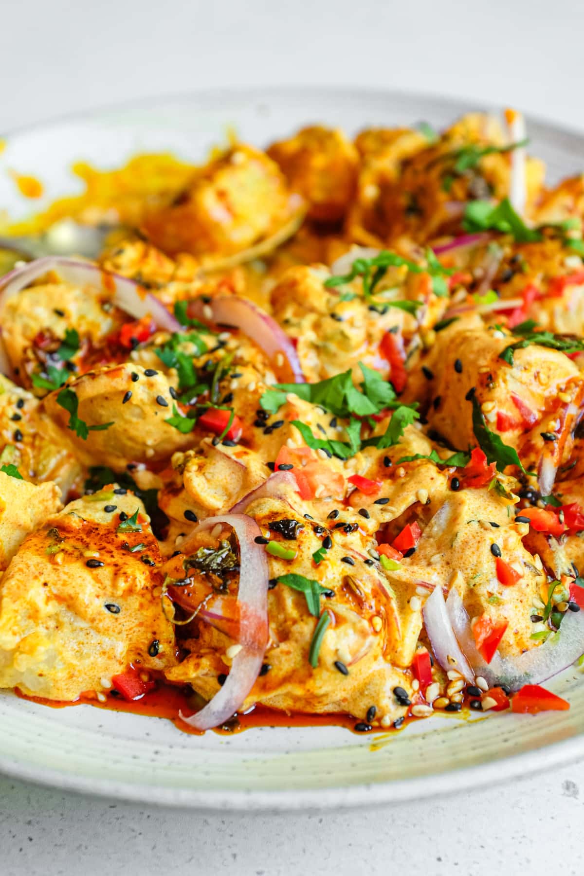 A close up image of a platter of creamy Aloo Chukauni, a Nepali potato and yoghurt salad garnished with a vibrant spiced oil