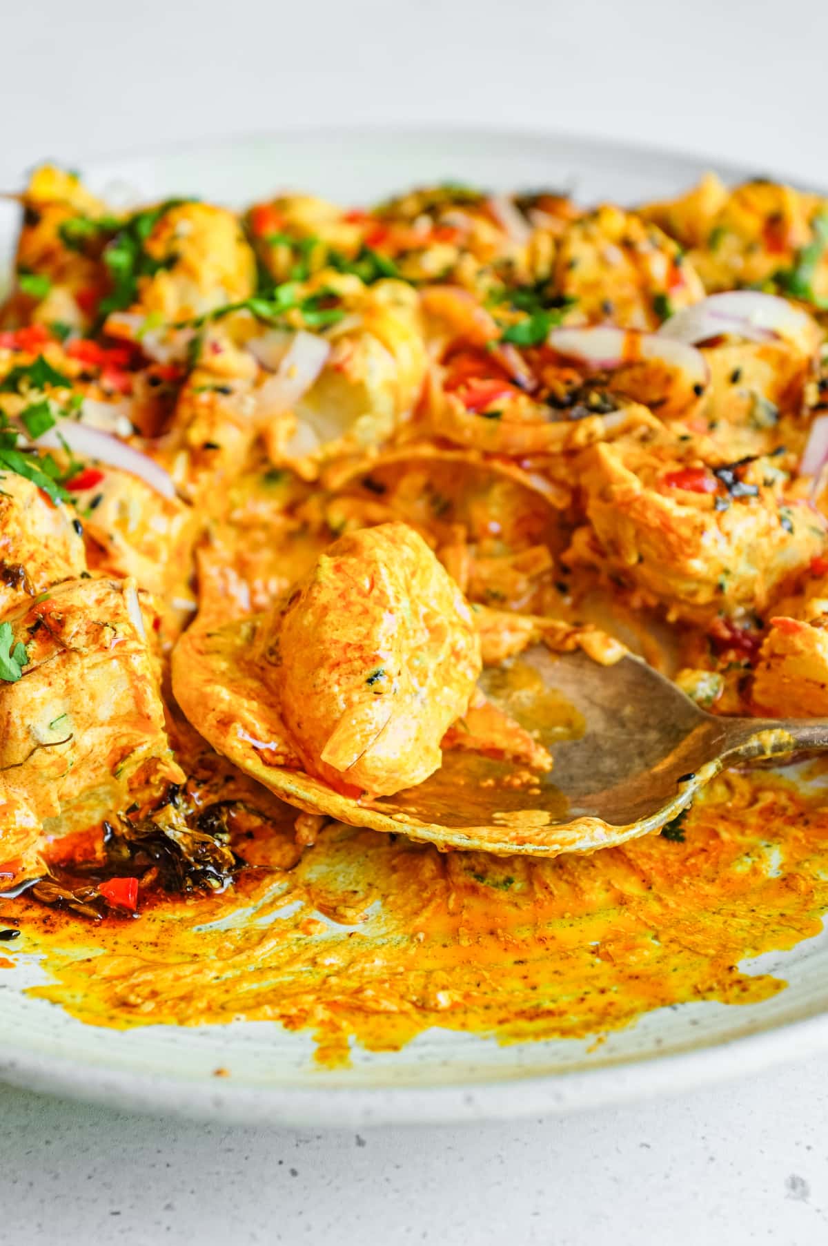 A close up image of a platter of creamy Aloo Chukauni with a spoon, a Nepali potato and yoghurt salad garnished with a vibrant spiced oil