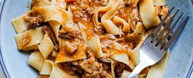 An overhead shot shows a bowl of duck ragù blended with pappardelle pasta ribbons.