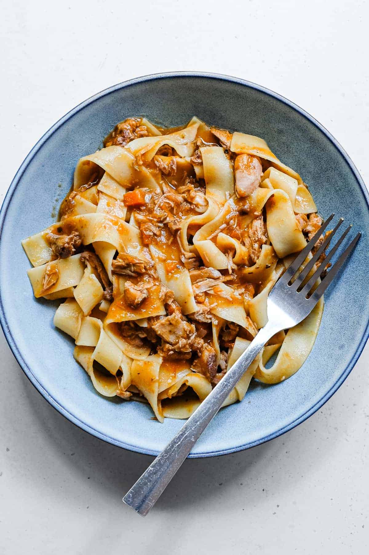 An overhead shot shows a bowl of duck rag&ugrave; blended with pappardelle pasta ribbons.
