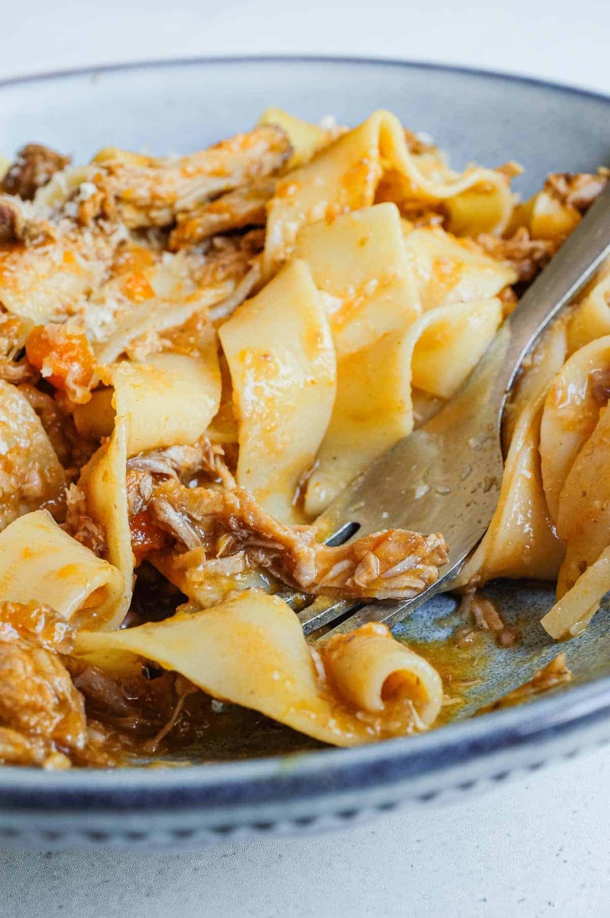 A fork sits in a bowl of pappardelle pasta tossed in a sauce from the Central region made from duck legs.