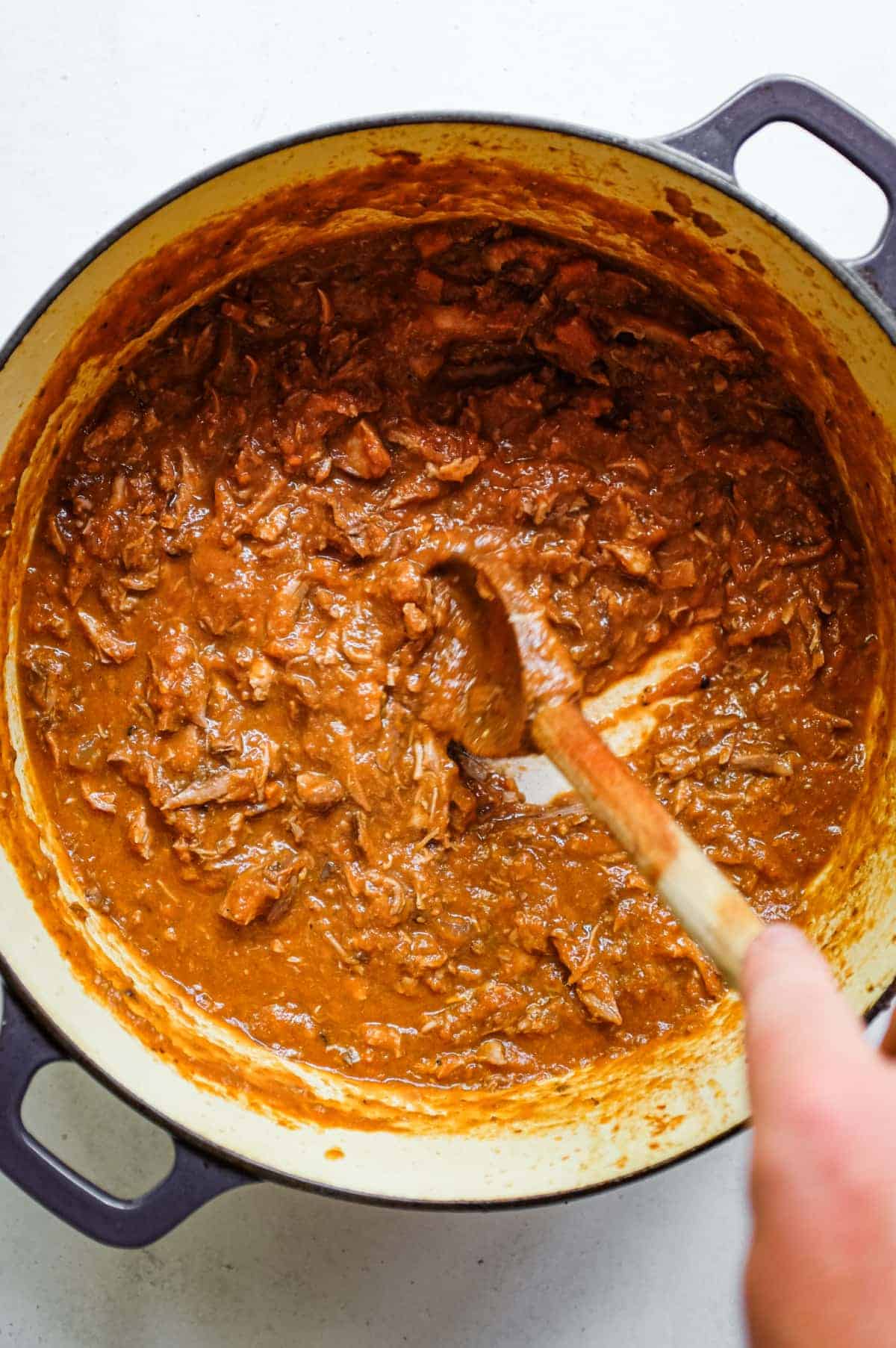 Duck Ragù with Pappardelle | cookeatworld.com A spoon stirs the thick, glossy duck ragù in a cast iron pot.
