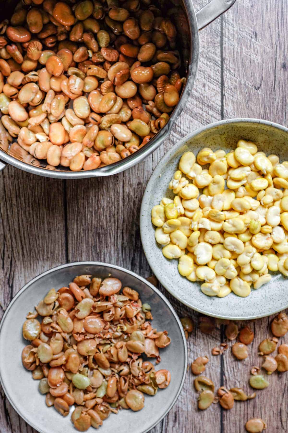 Three bowls, the top one containing soaked fava beans the middle skinned fava beans and the bottom bowl the skins of the beans.