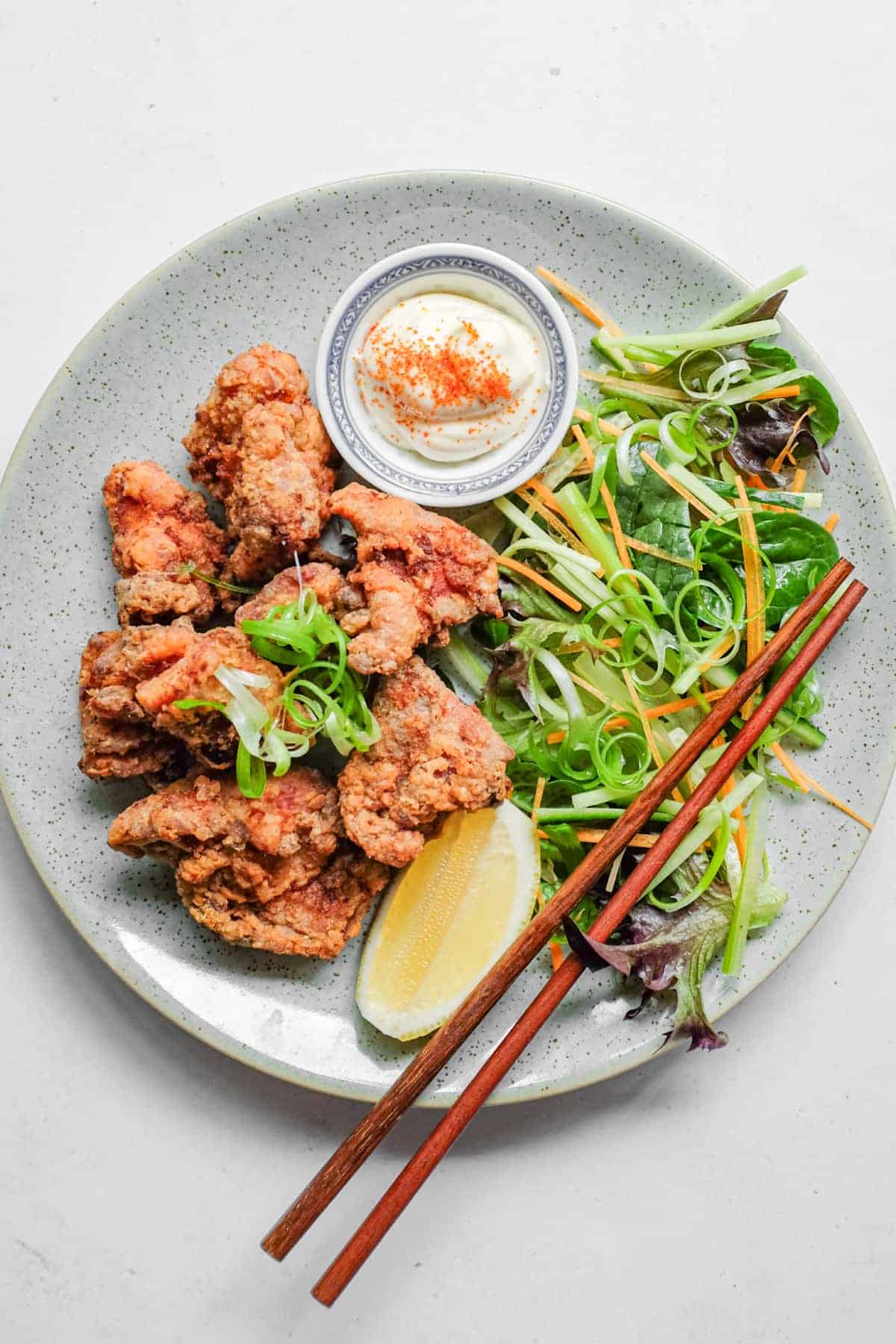 A plate of Japennese karaage chicken with a side salad, lemon wedge, and mayonnaise