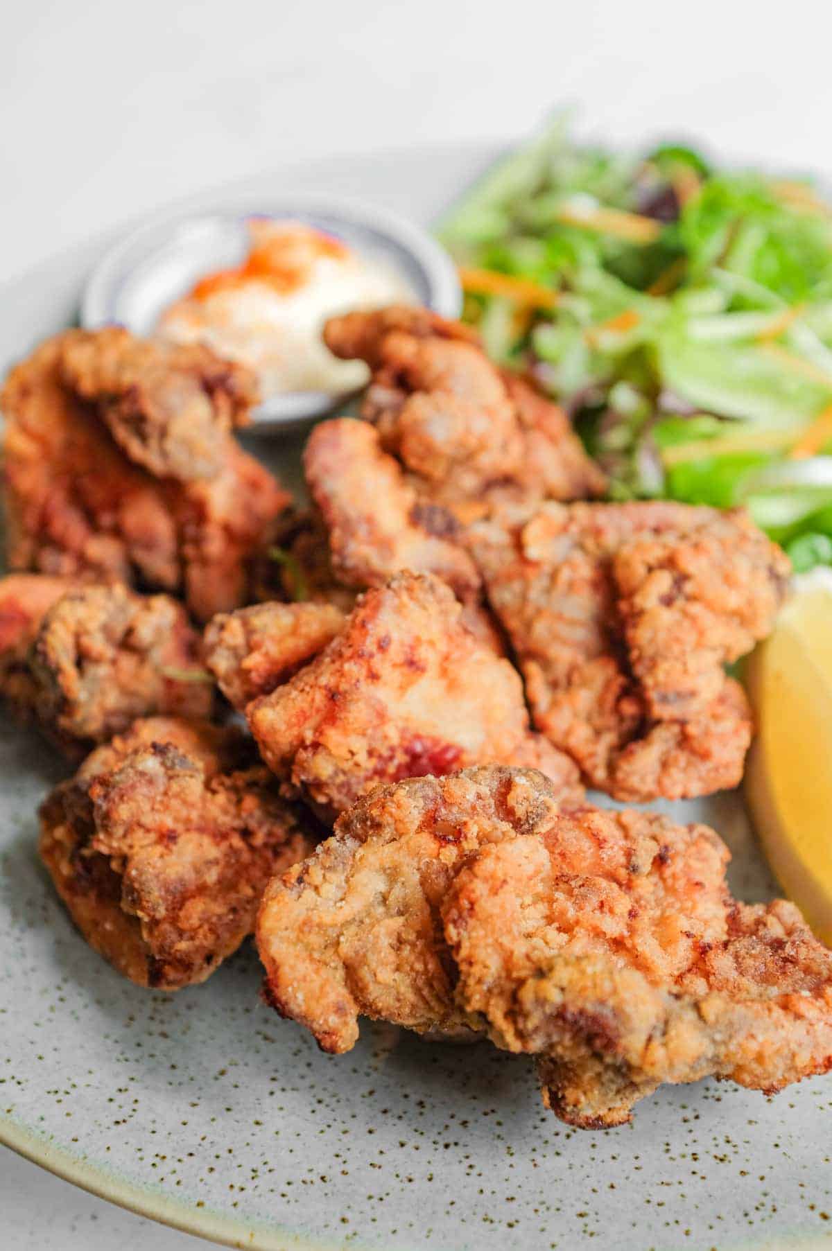 A plate of Japennese karaage chicken with a side salad, lemon wedge, and mayonnaise
