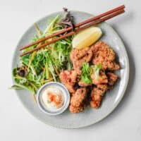 A plate of Japennese karaage chicken with a side salad, lemon wedge, and mayonnaise