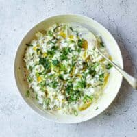 Bowl of cooling cucumber raita with spring onions and aromatic mustard oil