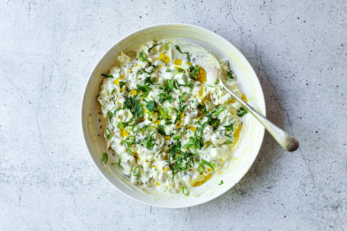 Bowl of cooling cucumber raita with spring onions and aromatic mustard oil