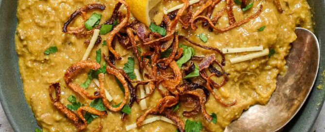 Bowl of thick haleem with lemon wedge, mint and cilantro garnish