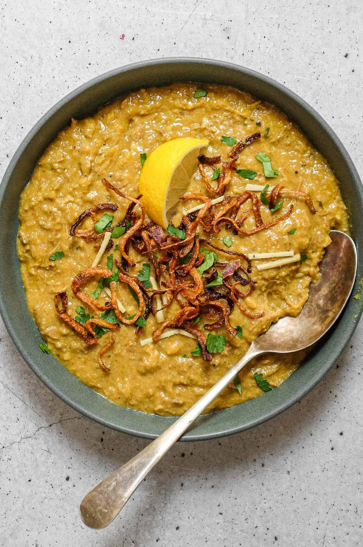 Bowl of thick haleem with lemon wedge, mint and cilantro garnish