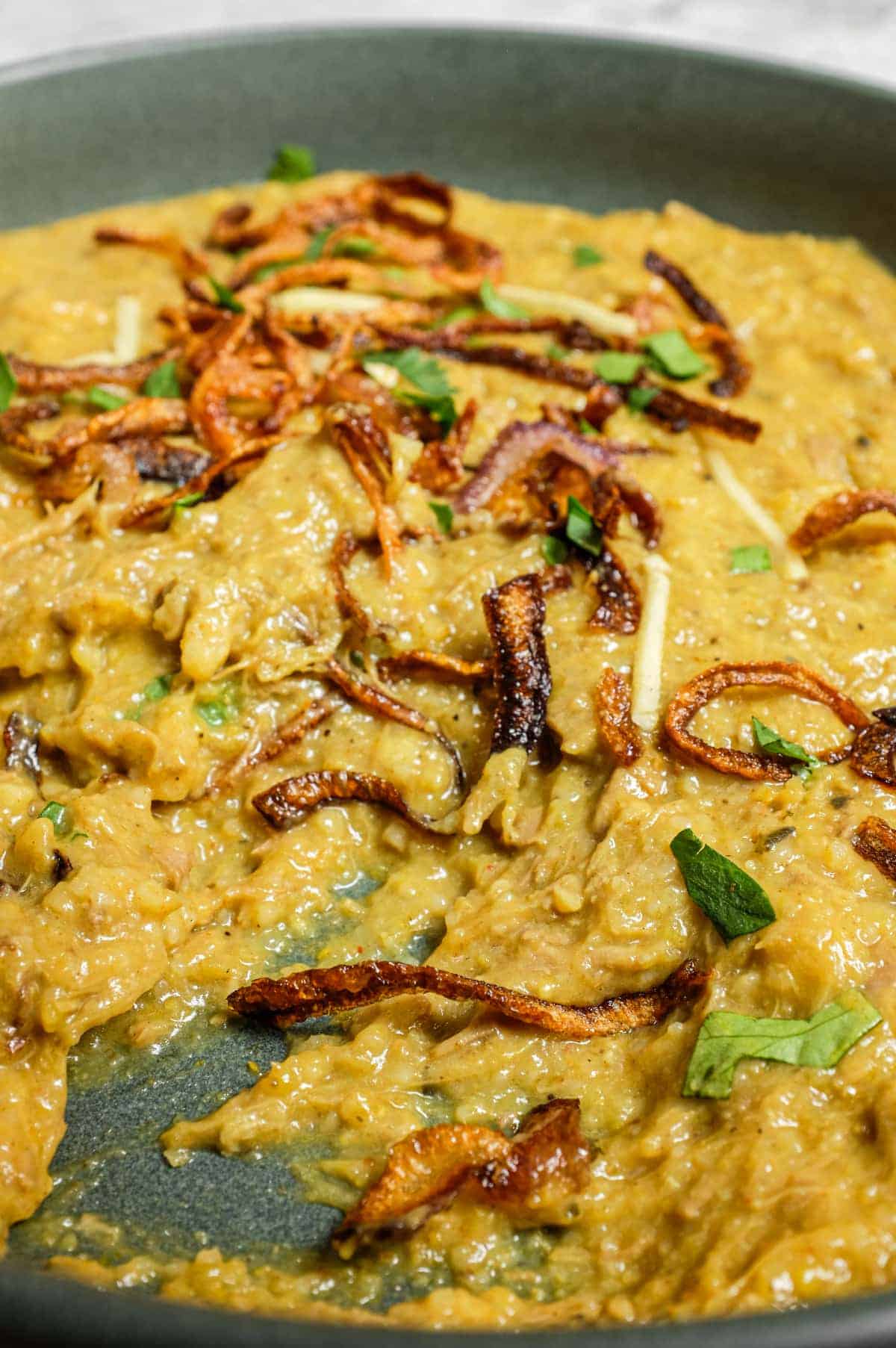 Silky haleem in a bowl with mint, crispy onions and a squeeze of lemon