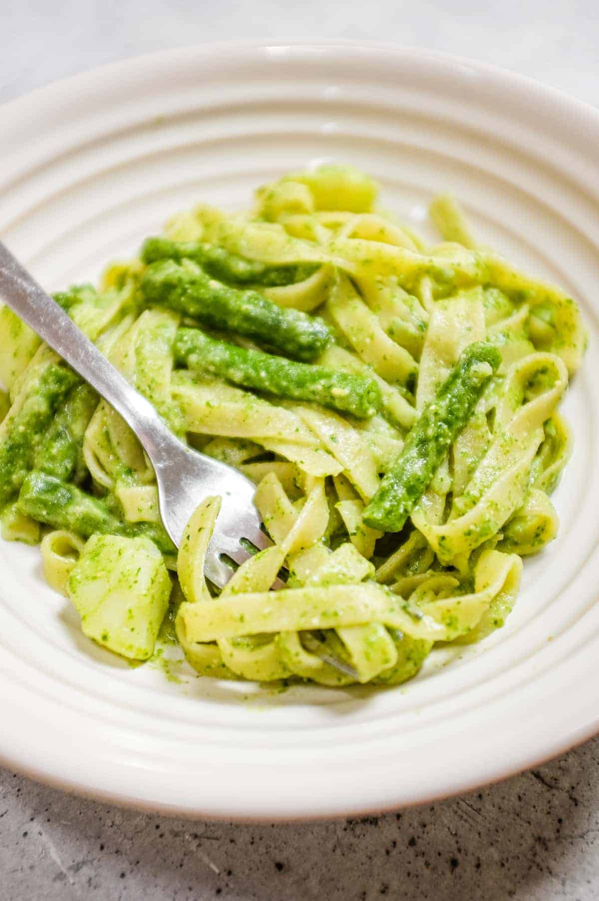 Bowl of pesto pasta coated in basil sauce with potatoes and beans