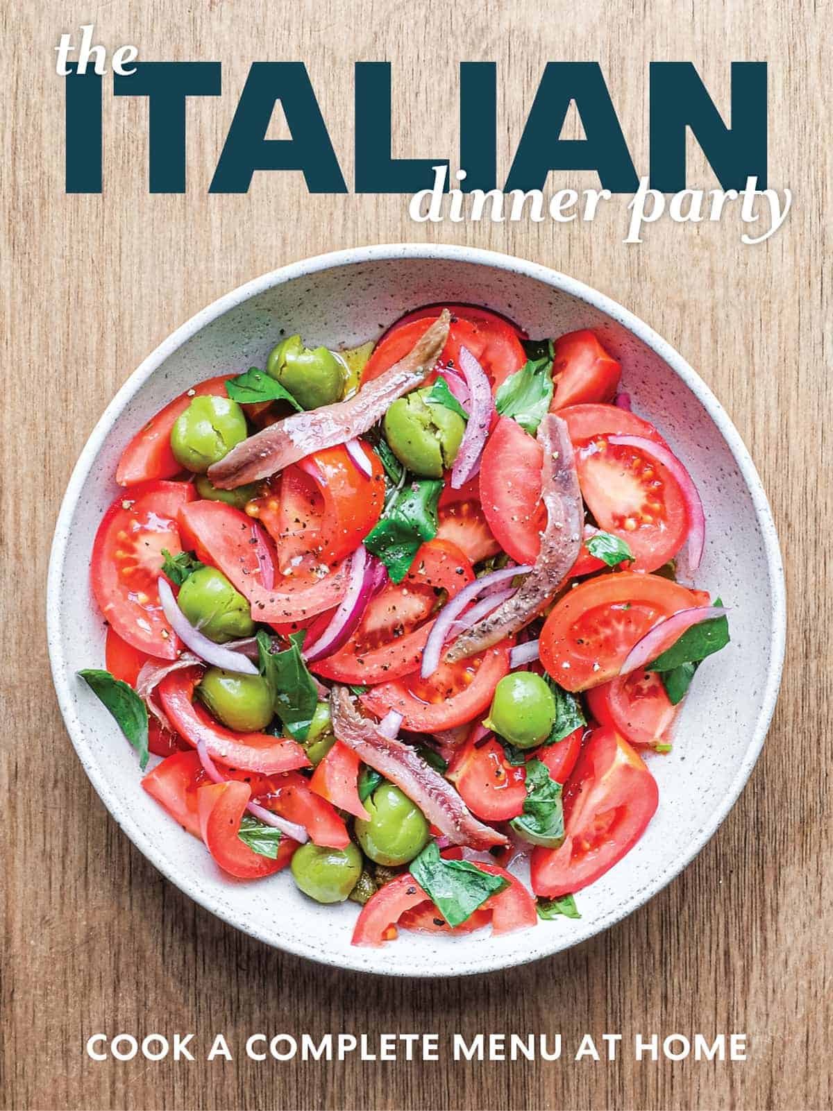 Italian dinner party book cover featuring a fresh tomato salad with olive oil, herbs and rustic styling on a serving plate.