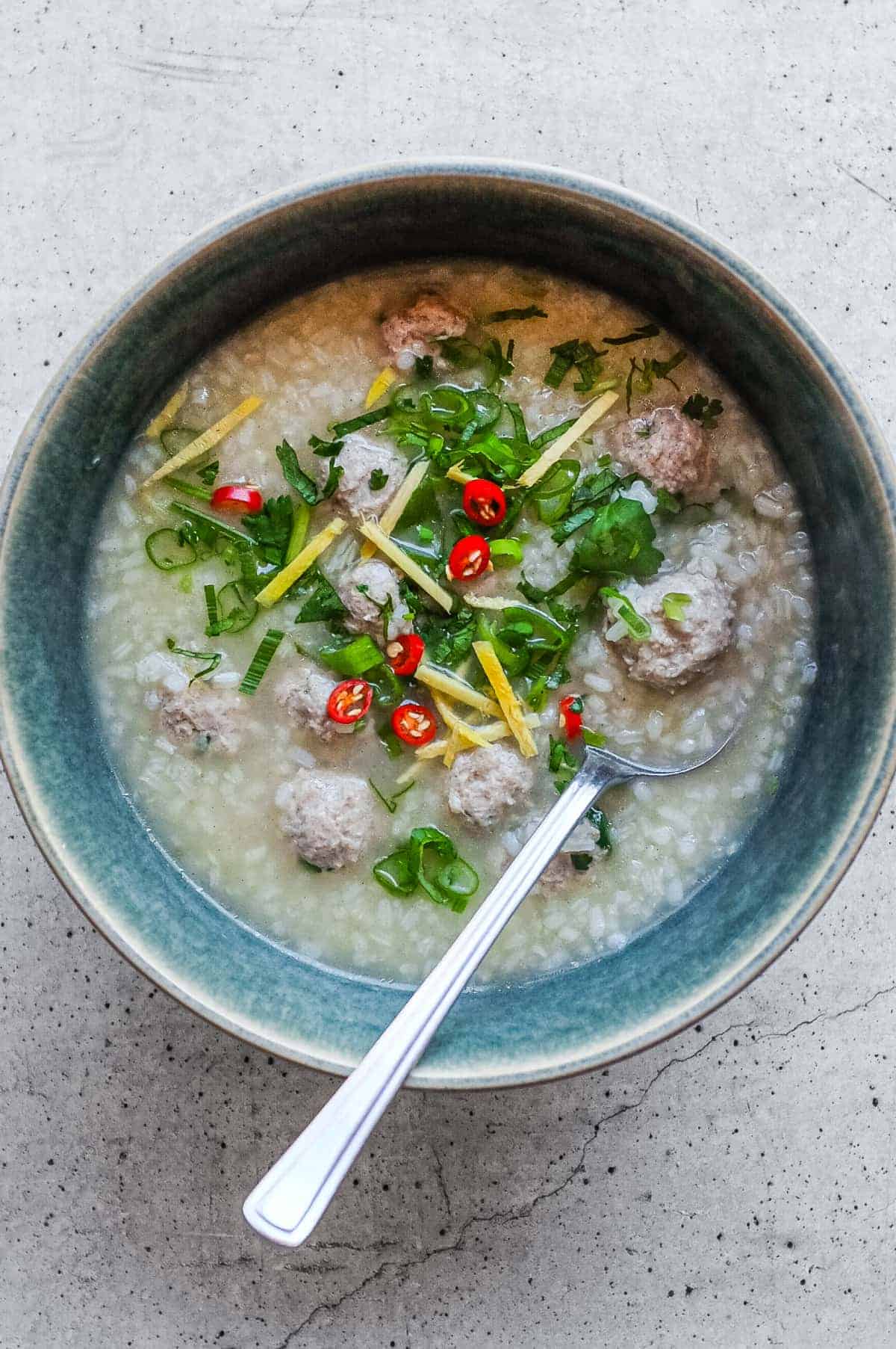 Bowl of Thai khao tom moo with pork meatballs, soft rice, coriander, ginger, chillies and sliced spring onions