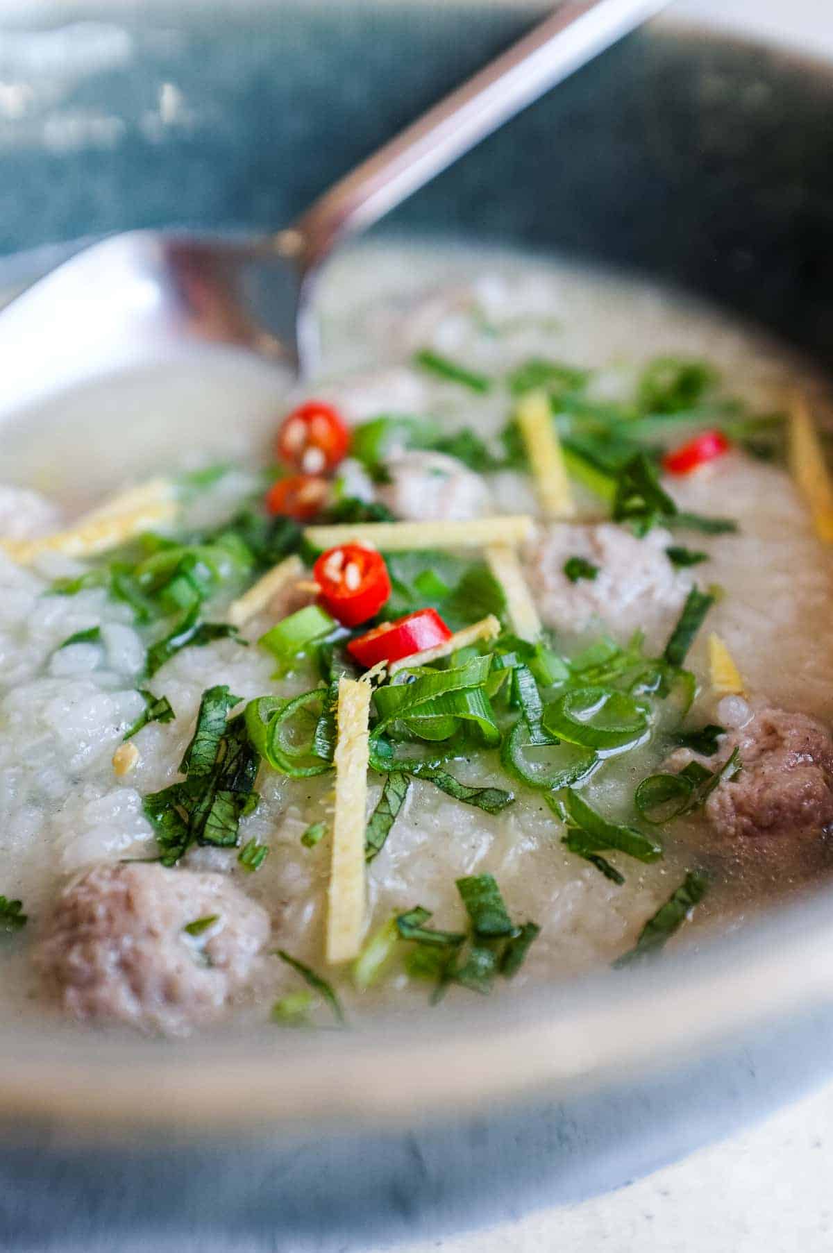 Close-up of seasoned pork meatballs and broken rice in a clear Thai garlic and coriander broth