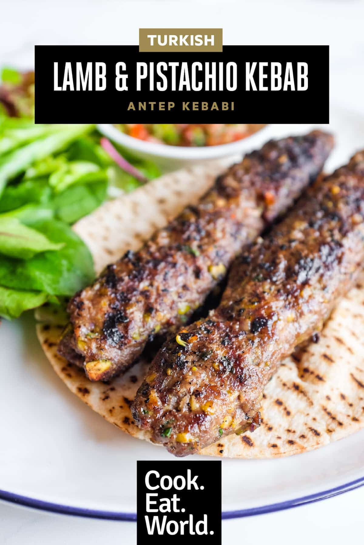 Close-up of a Turkish lamb köfte kebab with pistachios, spoon salad and mixed leaves.