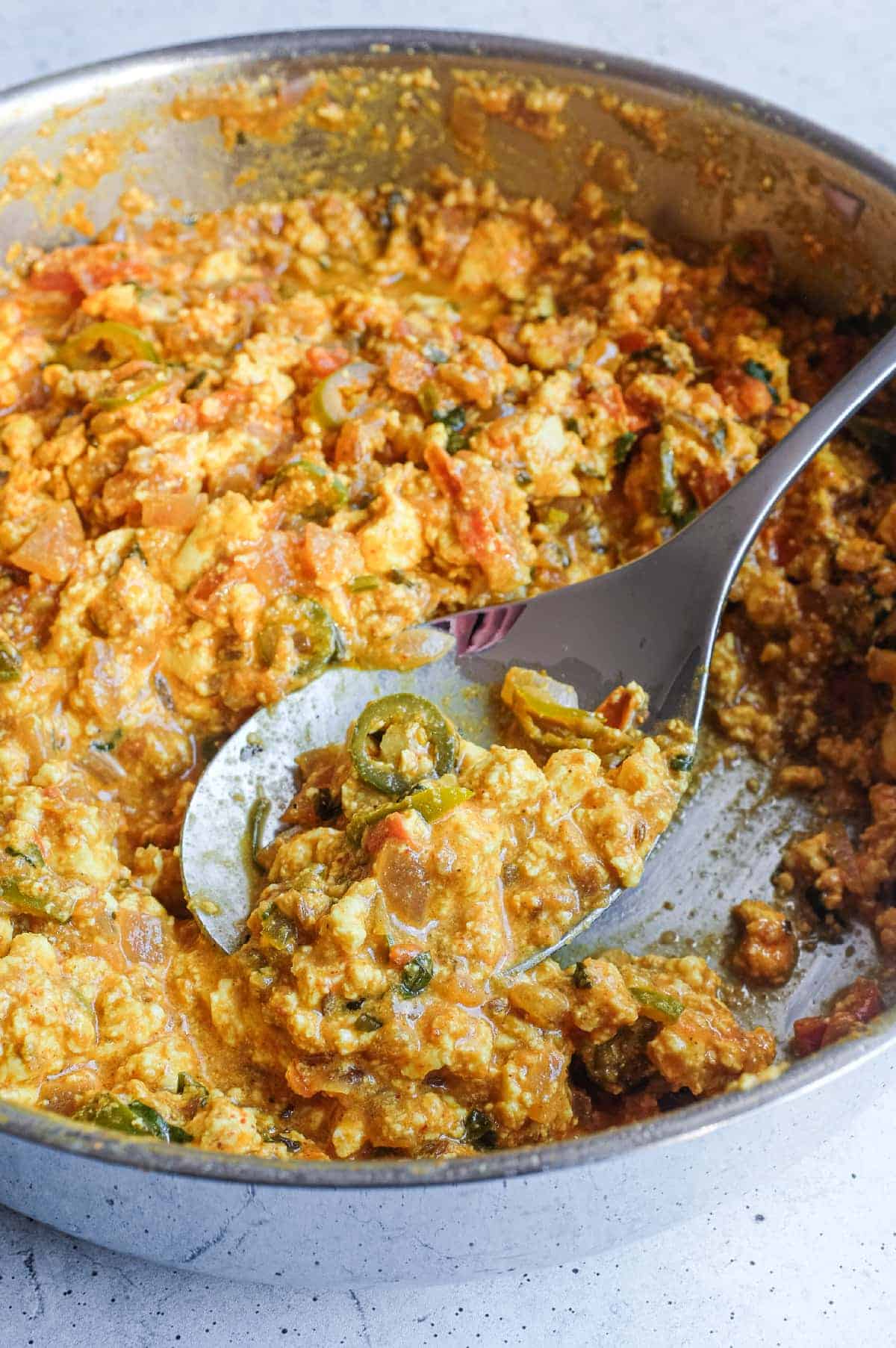 Indian scrambled paneer cooked in a rich tomato masala in a pan.