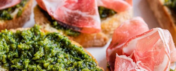A platter of Sicilian pistachio pesto crostini with some topped with prosciutto ham.
