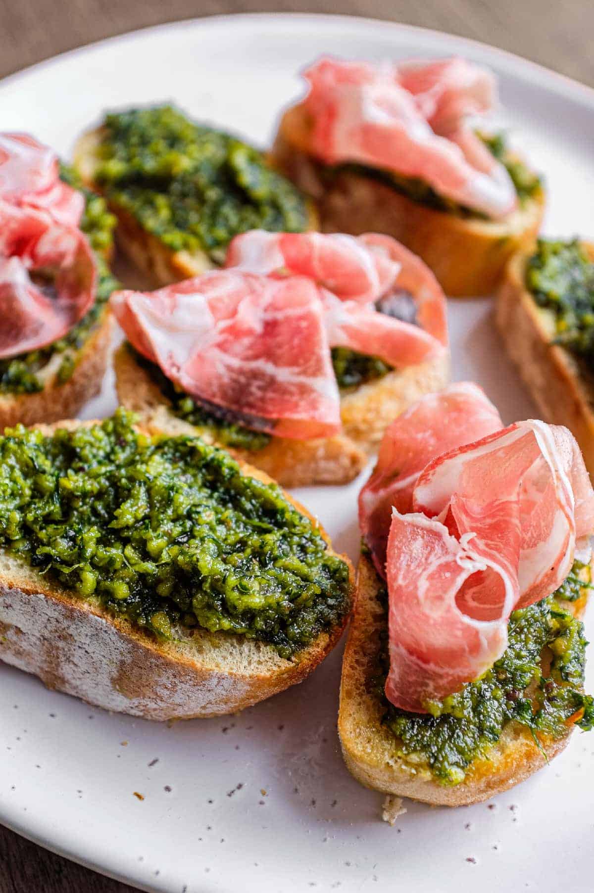A platter of Sicilian pistachio pesto crostini with some topped with prosciutto ham.
