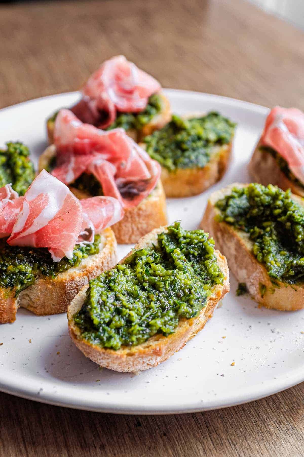 Homemade Sicilian pistachio pesto crostini served on a platter with optional prosciutto.