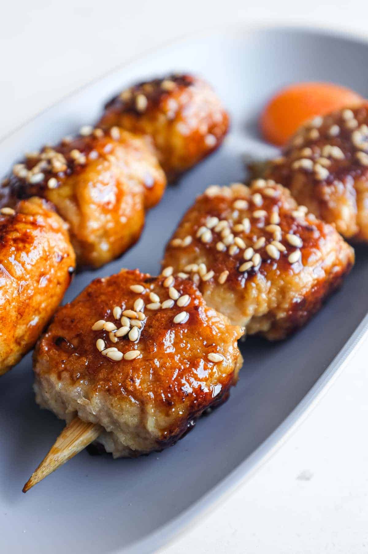Pan-fried tsukune skewers served with extra tare sauce and toasted sesame seeds