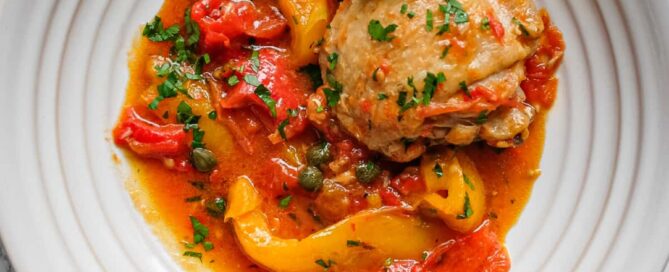 Close-up of chicken braised with colourful peppers and tomatoes in a rich sauce.