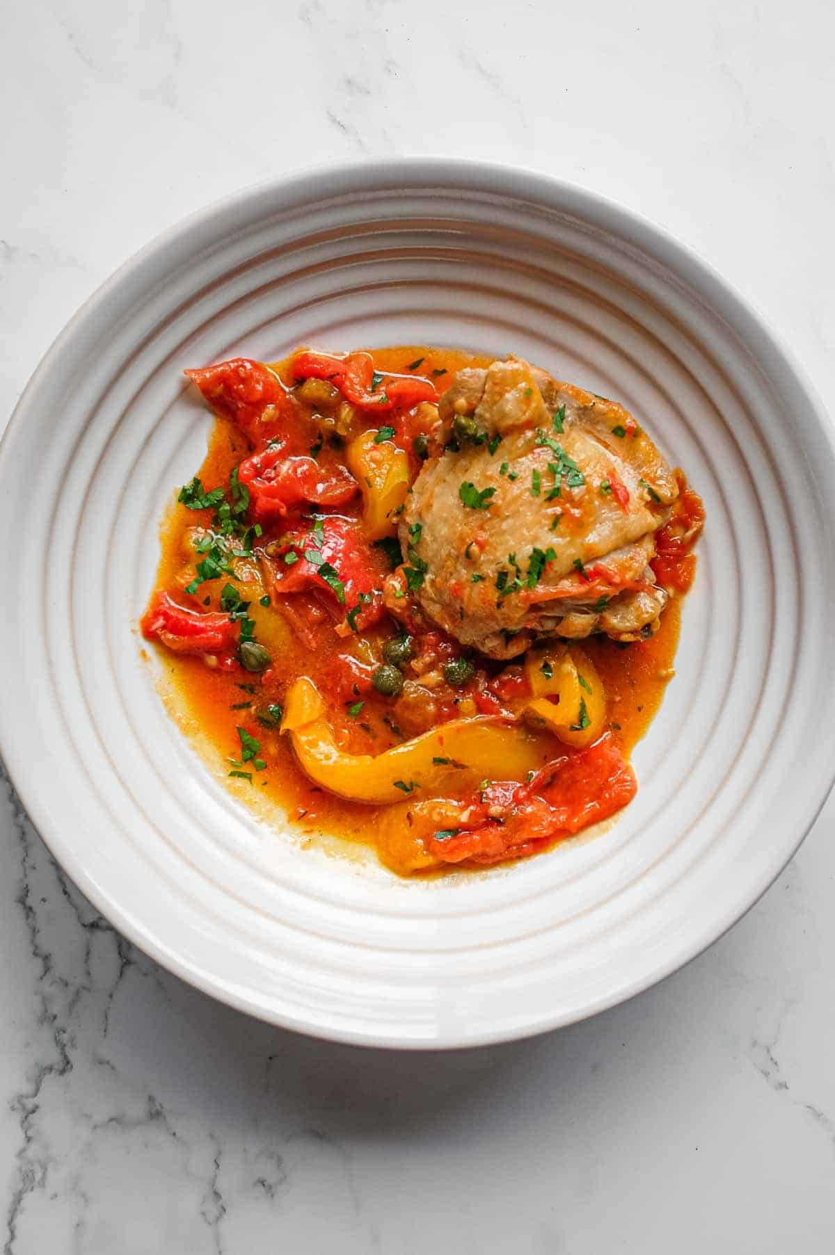 Close-up of chicken braised with colourful peppers and tomatoes in a rich sauce.