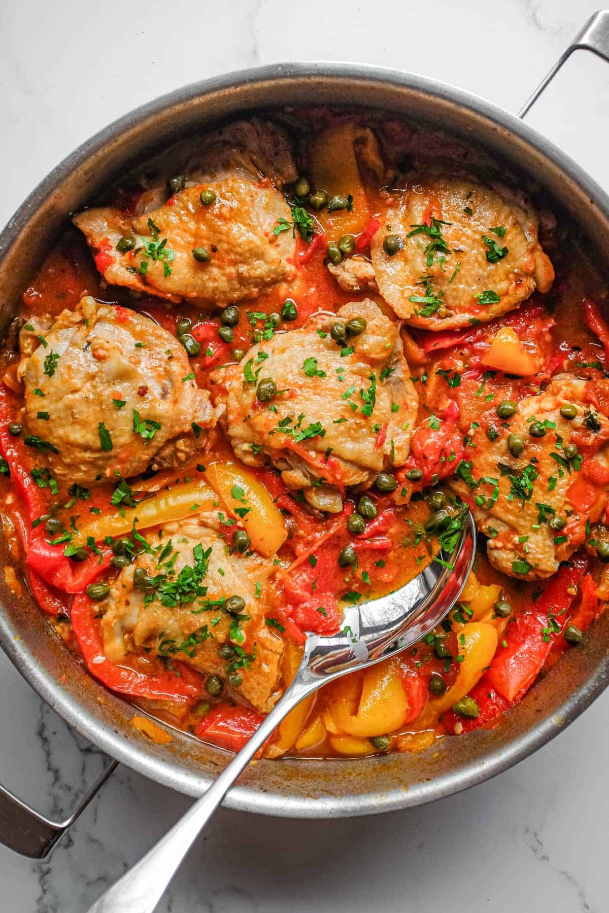 A pan of Roman chicken stew with tender chicken, sweet peppers, capers and chopped parsley.