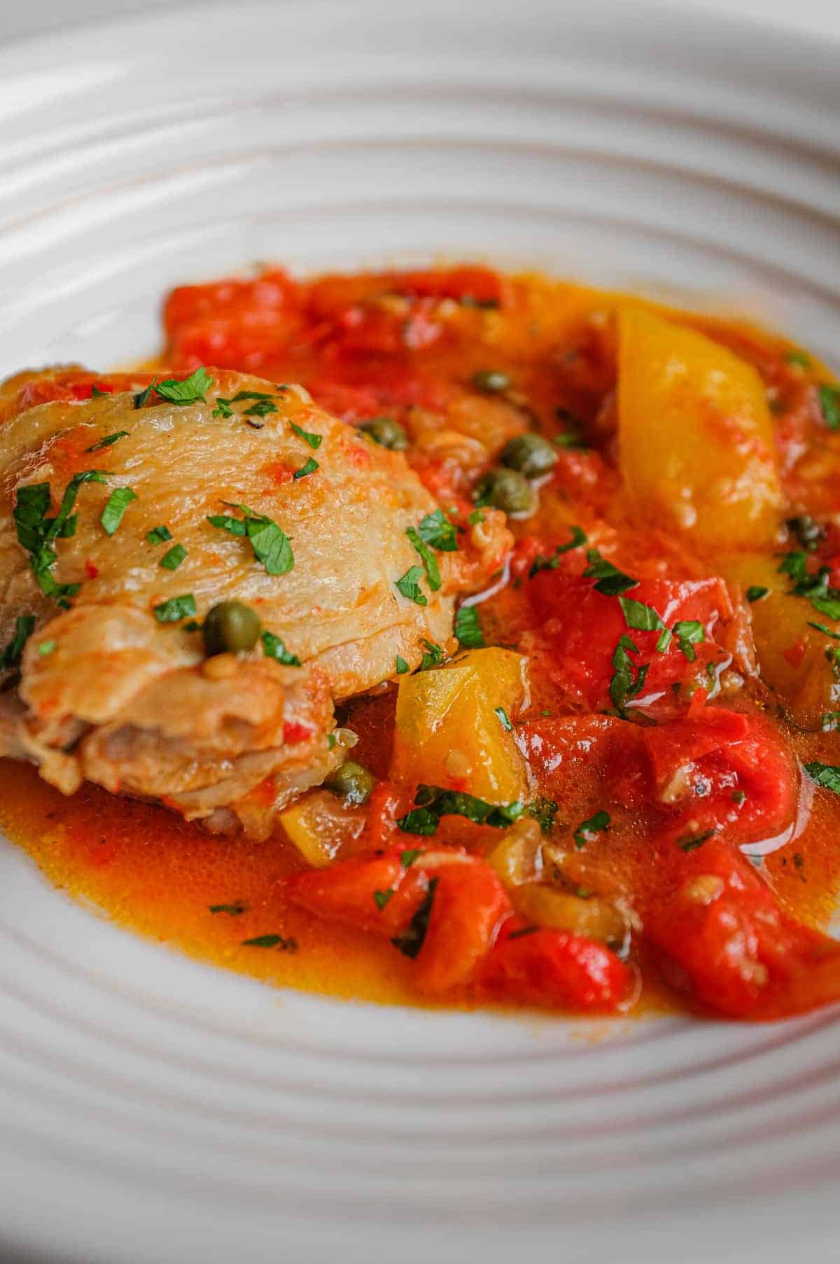 Close-up of pollo alla romana with chicken, red and yellow peppers and tomato sauce.
