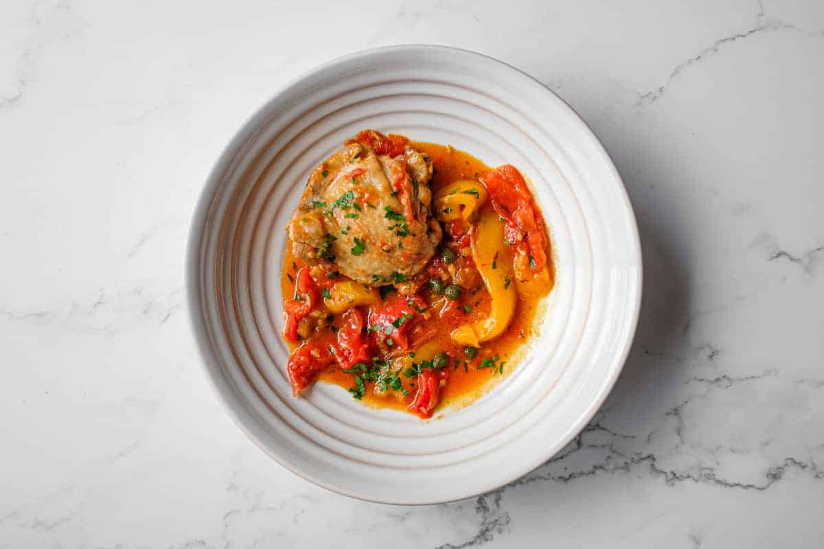 Overhead view of pollo alla romana with chicken, peppers, tomatoes and capers.