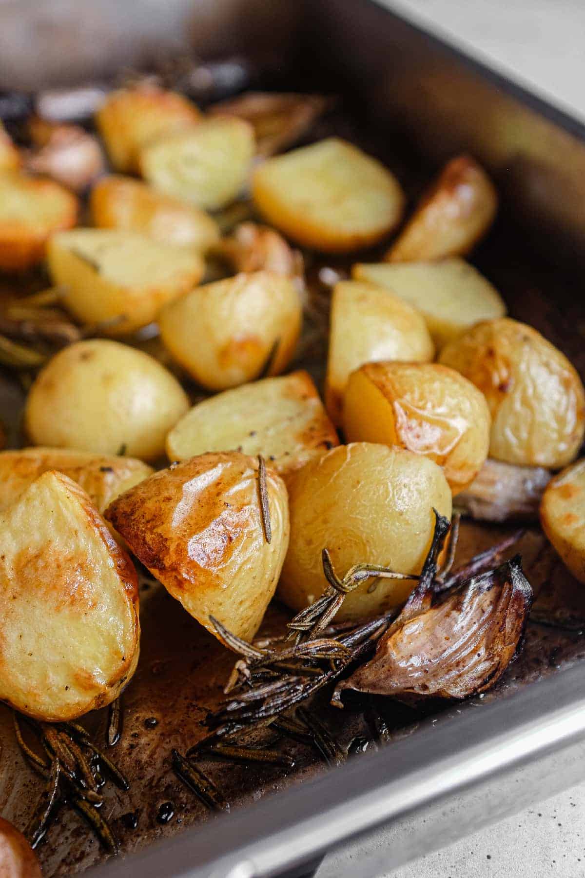 Patate al forno with rosemary and whole garlic cloves in a metal roasting tin.