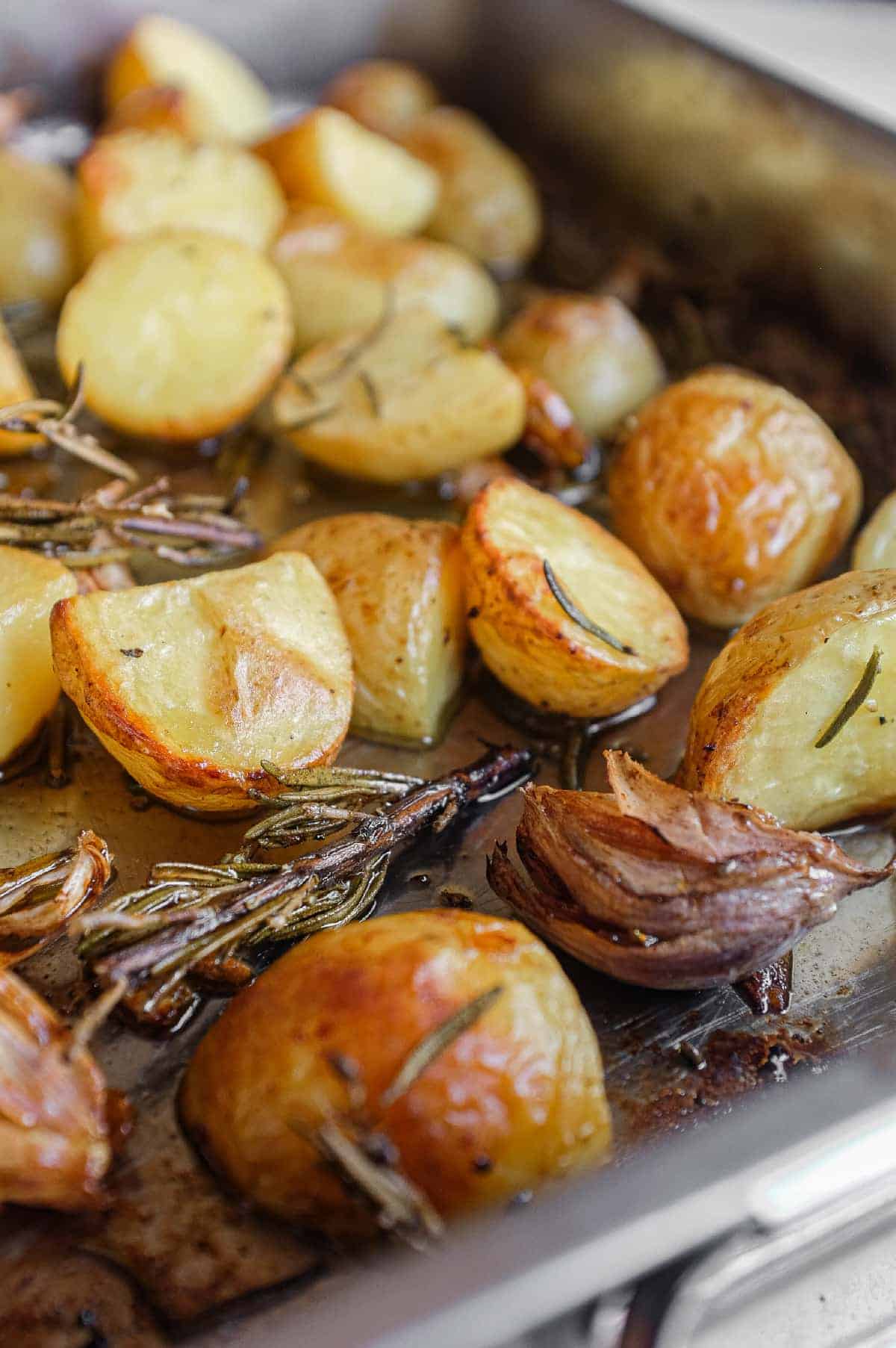 Italian-style roast potatoes with browned edges and fresh rosemary in a baking tin.